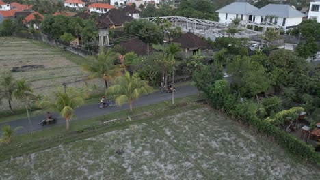 aerial orbits two cyclists riding on small road in rural cemagi, bali
