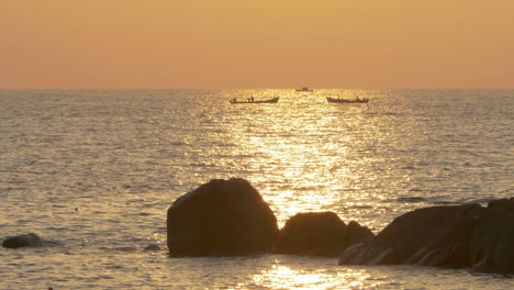 Silhouettes-of-Three-Fishing-Boats-with-Sea-Gull-Landing-on-Rock-at-Sunset,-Goa,-India