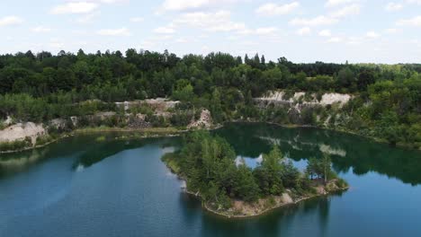 aerial view of lake with a small island and beautiful water in a quarry surrounded by forest tracking forward