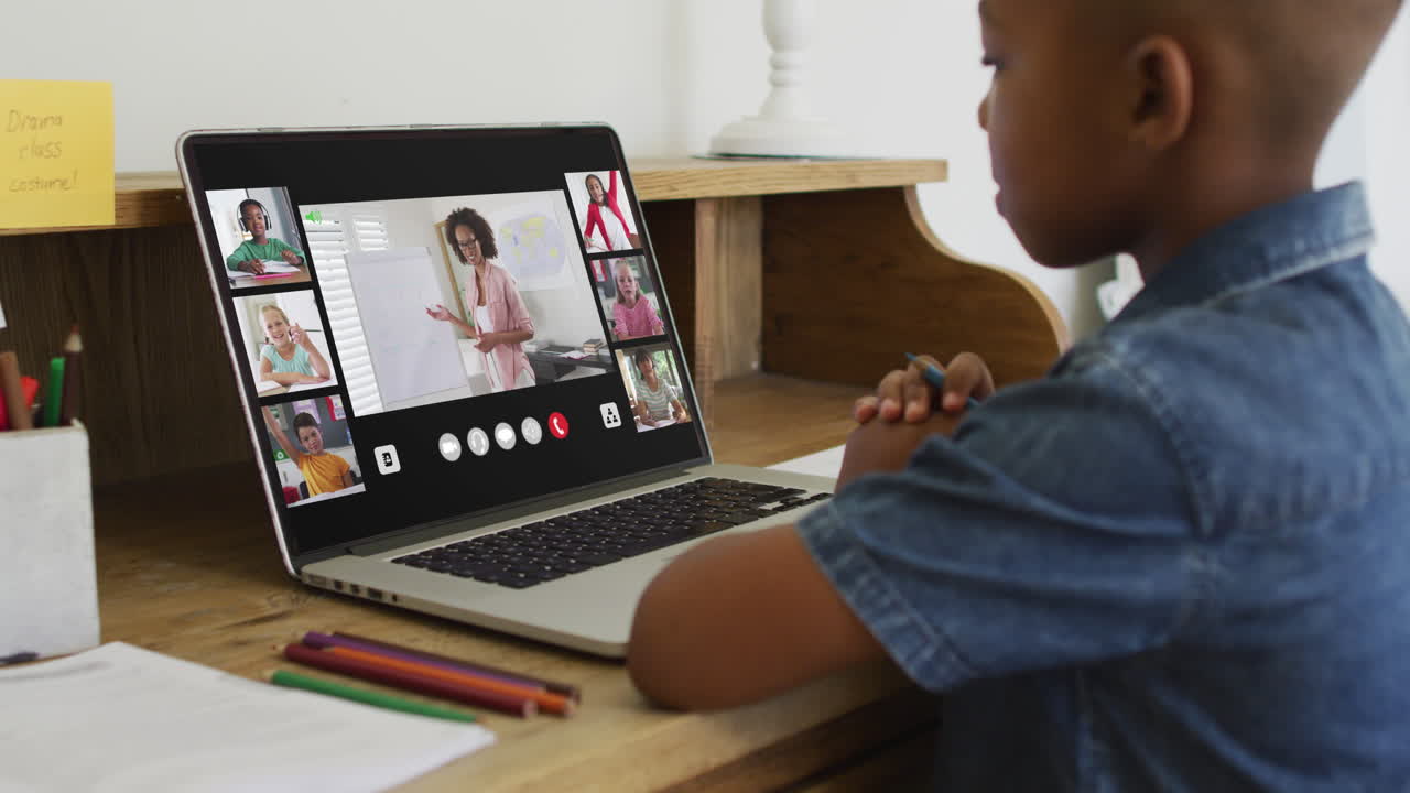 Schoolboy using laptop for online lesson at home, with diverse teacher and class on screen