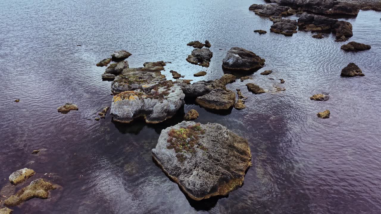 Luftfoto af klippefyldt kystlinje med roligt vand i skumringen