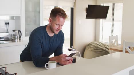 Caucasian-man-standing-in-kitchen-and-using-smartphone