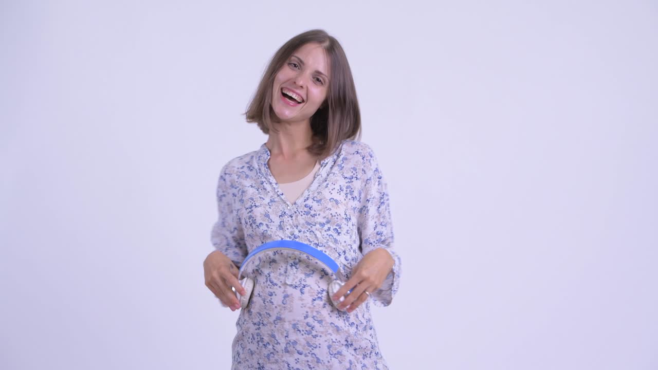 헤드폰을 들고 있는 행복한 젊은 아름다운 임신한 여자