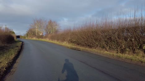 pov shot road bike ride cycling on sunny country lane shadow of cyclist in winter