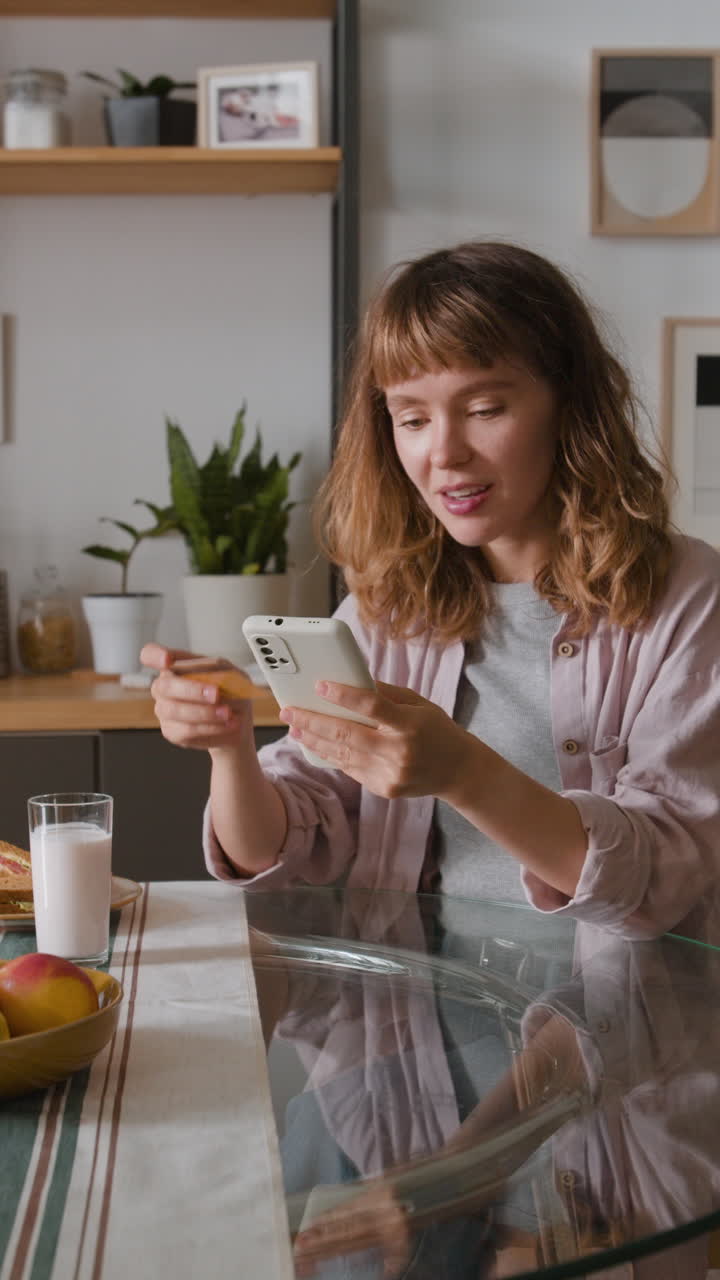 Woman using smartphone and credit card in kitchen
