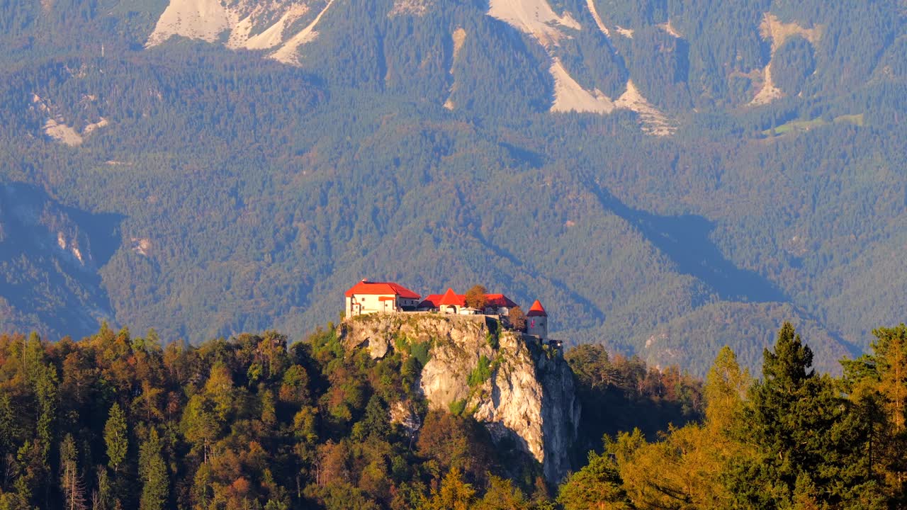 Parallax aerial tilt down reveals Bled island church and castle with mountains rising behind the lake, telephoto drone establishing