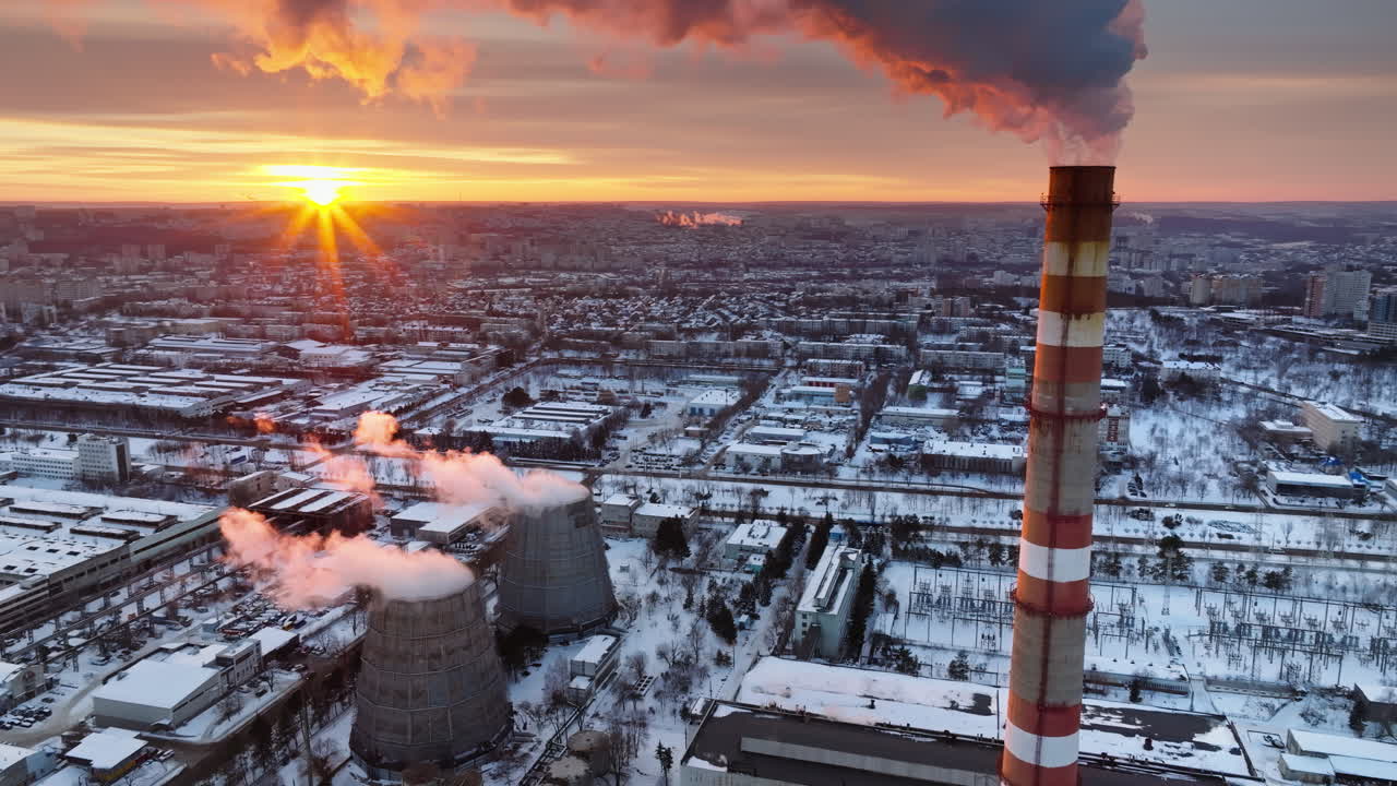 Aerial drone view of a working thermal power station in Chisinau at sunset. City covered in snow. Steam and smoke coming from pipes. Moldova