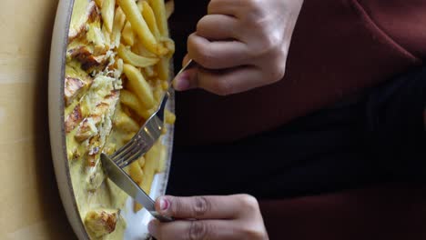 a woman eats a meal of chicken and fries with a fork and knife.