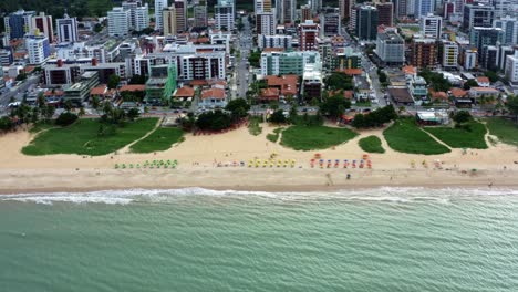 Right-trucking-aerial-drone-shot-of-the-famous-tourist-destination-Cabo-Branco-beach-in-the-tropical-capital-city-of-Joao-Pessoa-in-Paraiba,-Brazil-with-vibrant-tents-lined-up-for-visitors