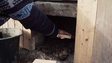 The-Man-is-Cleaning-Out-the-Interior-of-the-Stove-Situated-Beneath-the-DIY-Hot-Tub---Close-Up