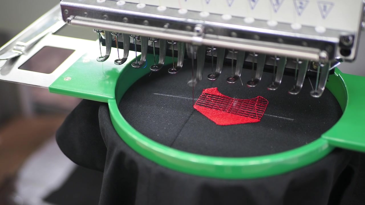 Macchina da ricamo industriale che ricama un disegno rosso su tessuto nero