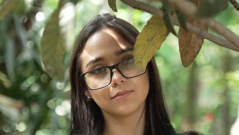 hermosa mujer latina de ojos verdes con gafas mirando a la cámara desde detrás de una rama en el parque