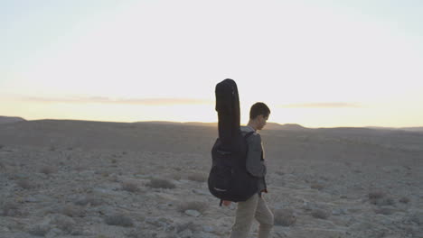 Young-man-walks-with-guitar-case-in-desert-sunset