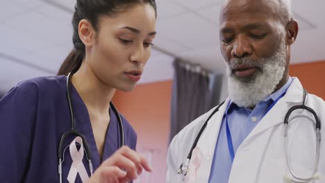 two diverse male and female doctors wearing cancer awareness ribbons talking at hospital