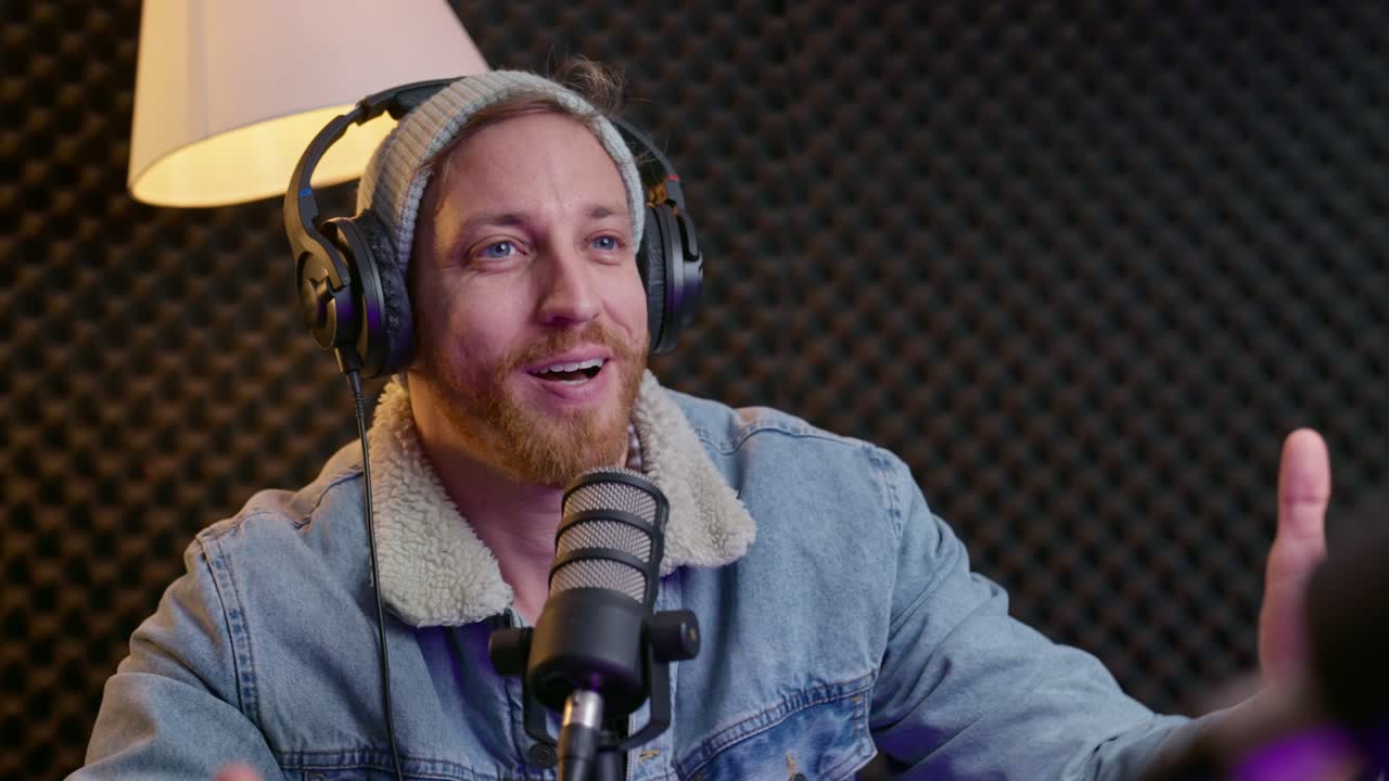 podcaster con auriculares entrevista a un invitado en un estudio profesional. ambos sentados en una mesa con micrófonos, teniendo una conversación. podcaster bebiendo de su taza de café mientras habla.