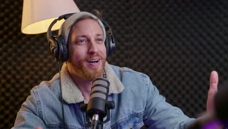 podcaster wearing headphones interviews a guest in a professional studio. both seated at a table with microphones, having conversation. podcaster sipping from his coffee mug while speaking.