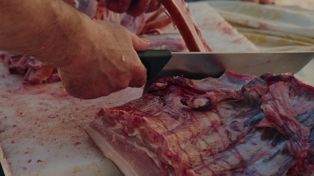 Man slicing pork ribs with cleaver during pig butchering in Portugal