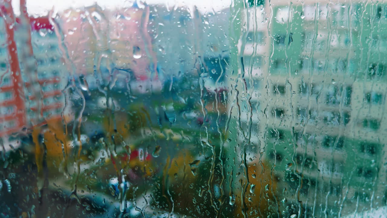 Glass of the window with rain water dripping down. Rainy day in the city from top floor of the flat.