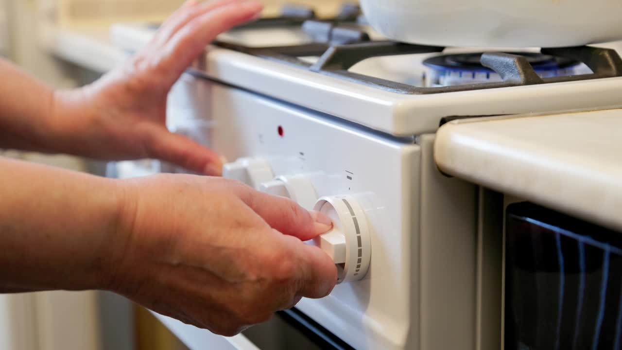 mani di una donna caucasica anziana che accende una stufa a gas domestica bianca con un bollitore smaltato bianco