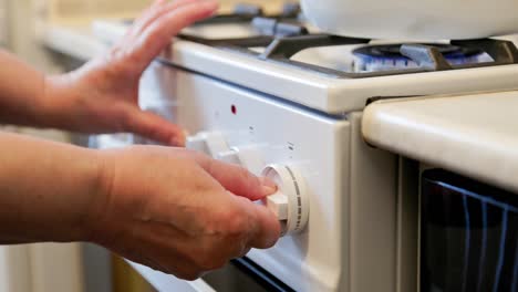 manos de una mujer caucásica anciana encendiendo una estufa de gas doméstica blanca con una tetera esmaltada blanca