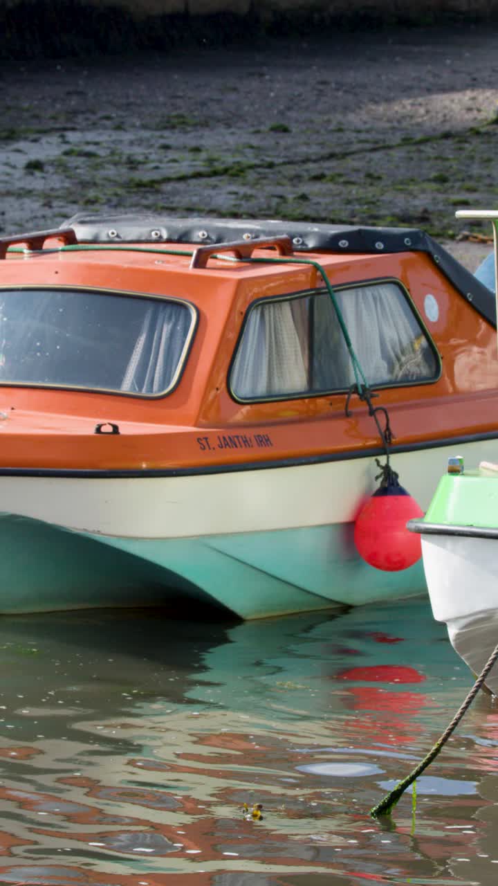 Motoscafo arancione e verde acqua che galleggia su acque calme del porto, luce diurna, lento movimento laterale della telecamera