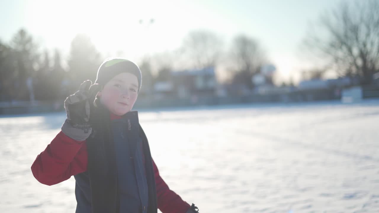 Slow-motion shot of a child in a red snowsuit giving the peace sign.