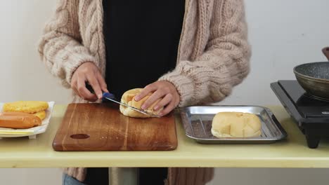 Frau-Schneidet-Brötchen-Auf-Schneidebrett-Und-Bereitet-Sich-Darauf-Vor,-Chicken-Cheeseburger-Zuzubereiten