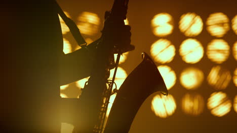 las manos de la silueta del saxofonista tocando un instrumento musical en los reflectores de cerca.