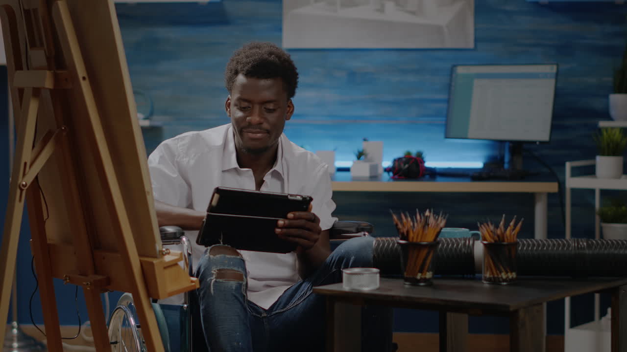 Black artist sitting in wheelchair using digital tablet