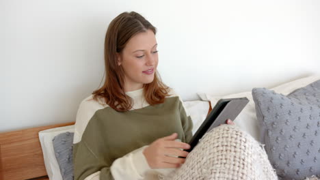 Relaxing in bed, woman reading on tablet and enjoying cozy blanket