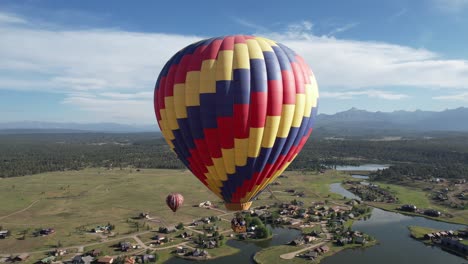 Vista-Aérea-De-Coloridos-Globos-Aerostáticos-Que-Vuelan-Sobre-El-Paisaje-Verde-Y-El-Lago-En-Un-Día-Soleado-De-Verano