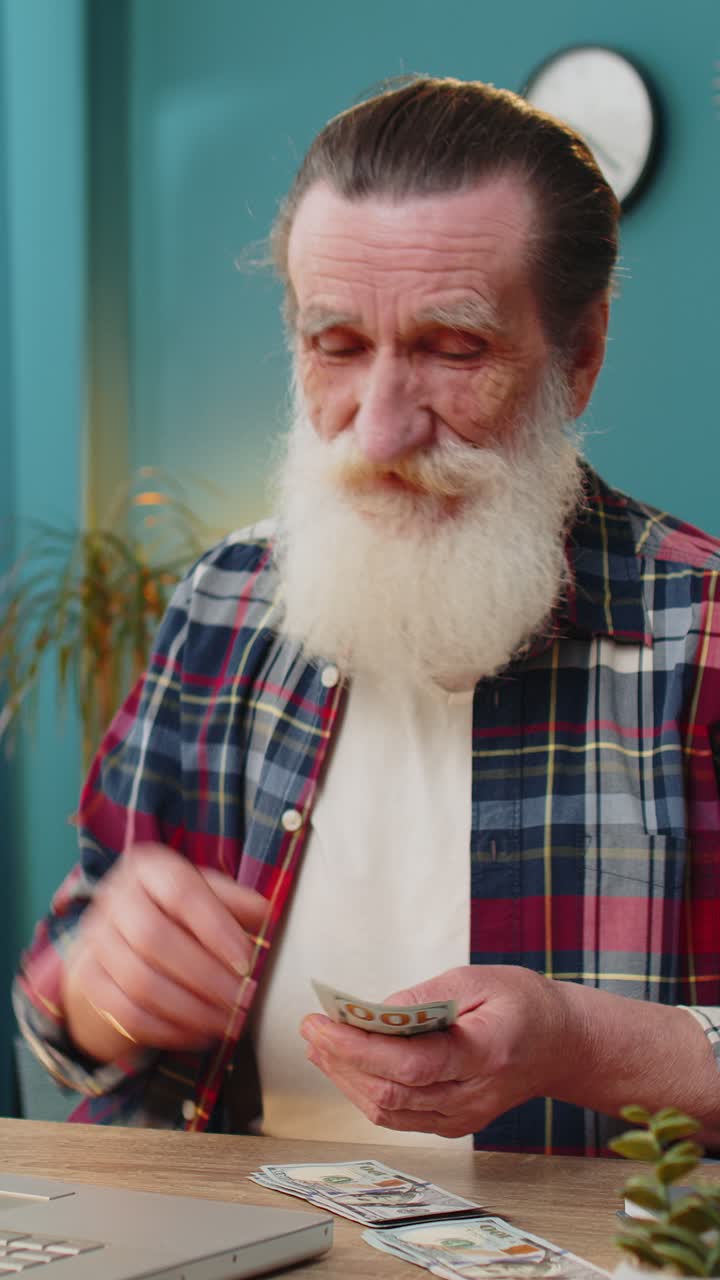 Senior man counting money cash calculates dividends profits salary and using laptop in home office
