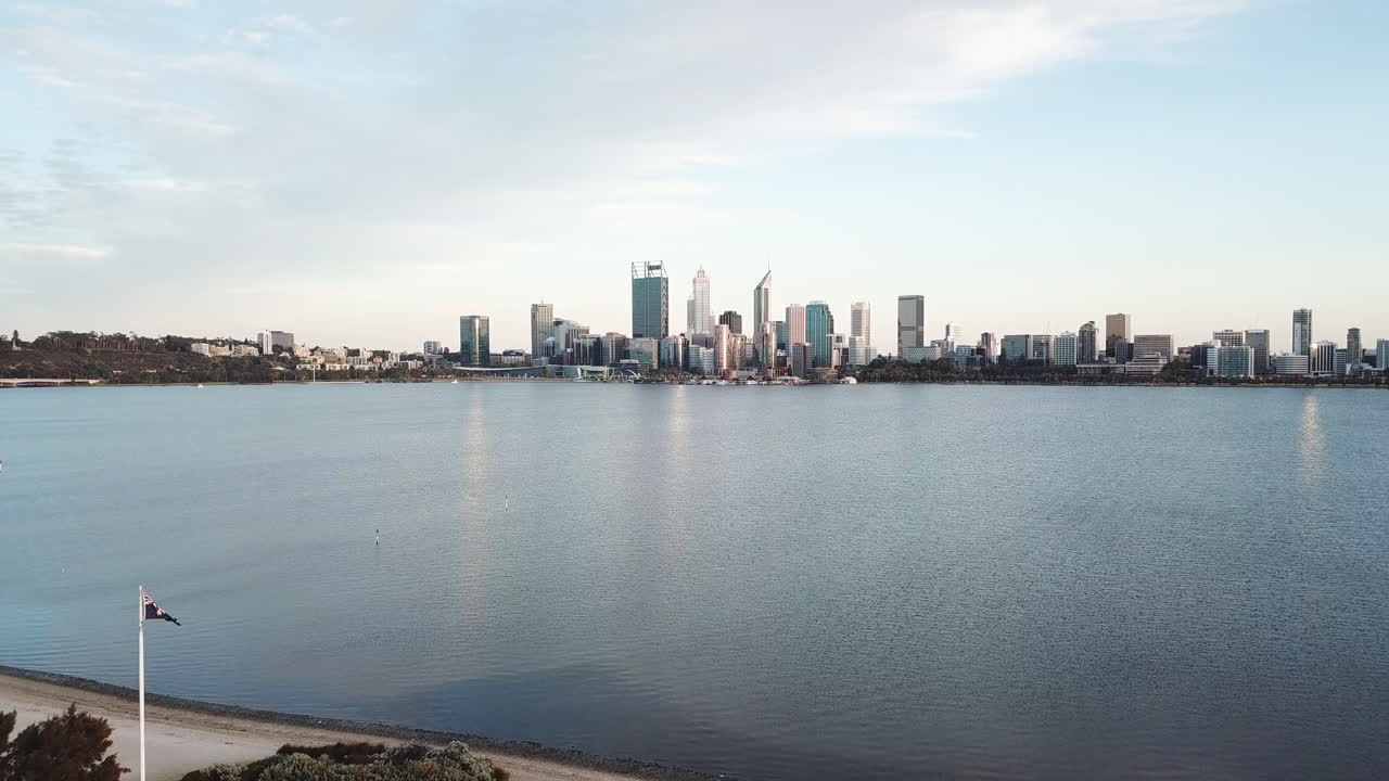Drone tracking straight over park and Australian National Flag, large city in background