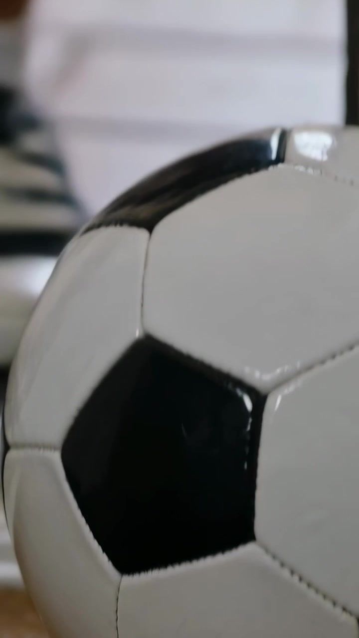 Video vertical: Balón de fútbol clásico rodando que entra en foco en casa mientras la vista cambia, espacio para texto.