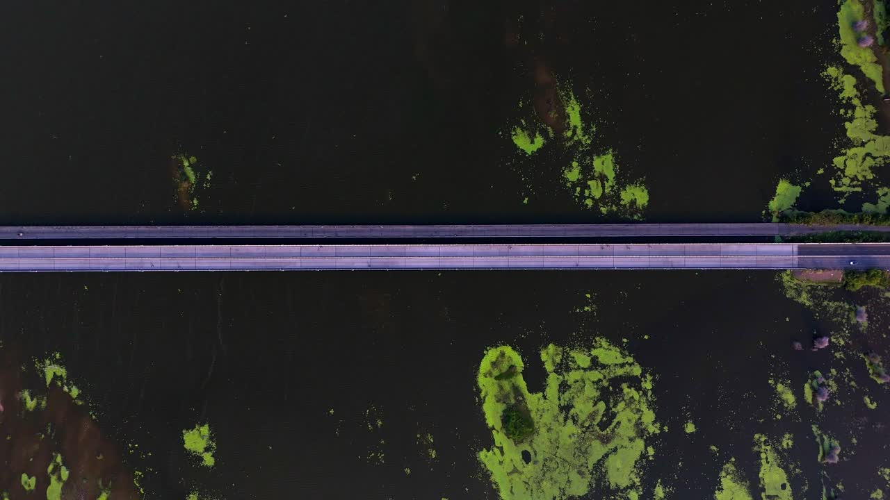 A unique aerial perspective of Chennai ECR's bridge over water, displaying light traffic and striking natural algae formations, a key scenic route. Very height aerial view of a bridge in Tamil Nadu