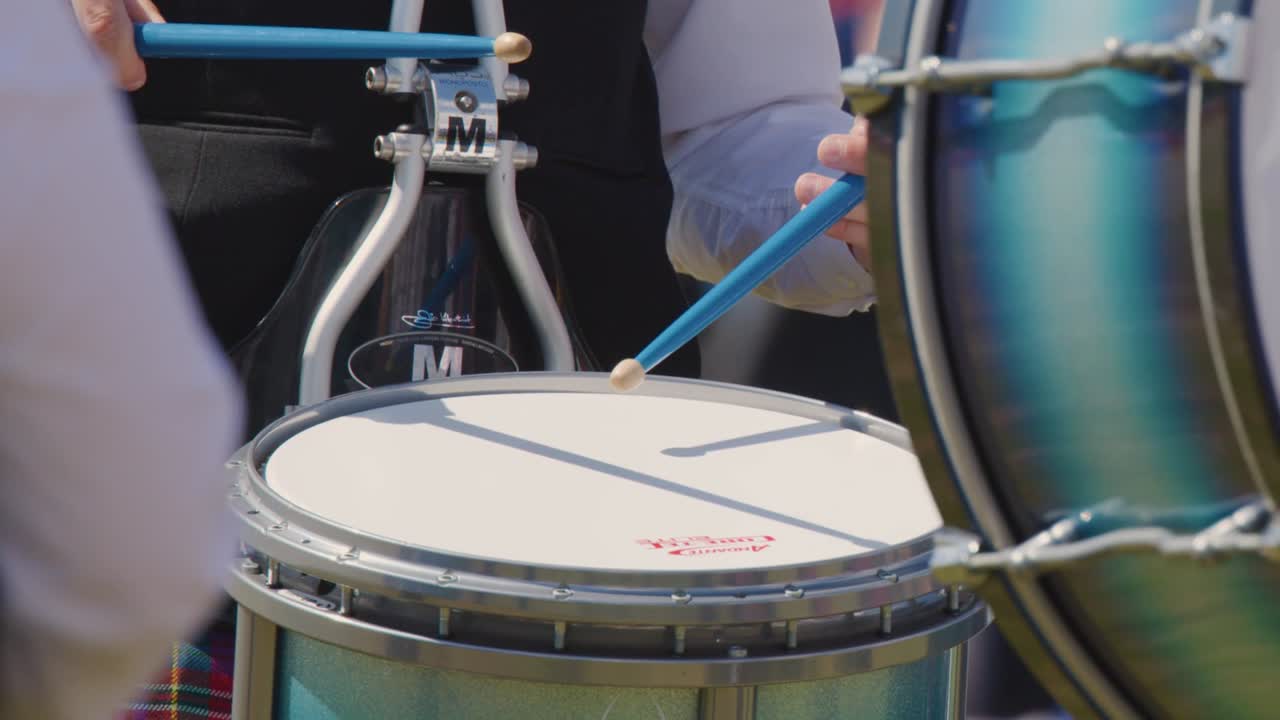 Detailed close-up of a musician's hands playing a snare drum with blue sticks during performance