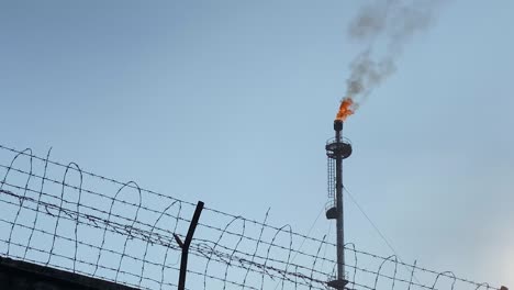 Feuer-Spuckt-Aus-Einem-Schornstein-Auf-Einer-Gasanlage,-Die-Hinter-Einem-Stacheldrahtzaun-Treibstoff-Verbrennt