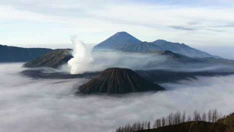 drone shot tilting toward smoking crater in middle of fog, sunrise in indonesia