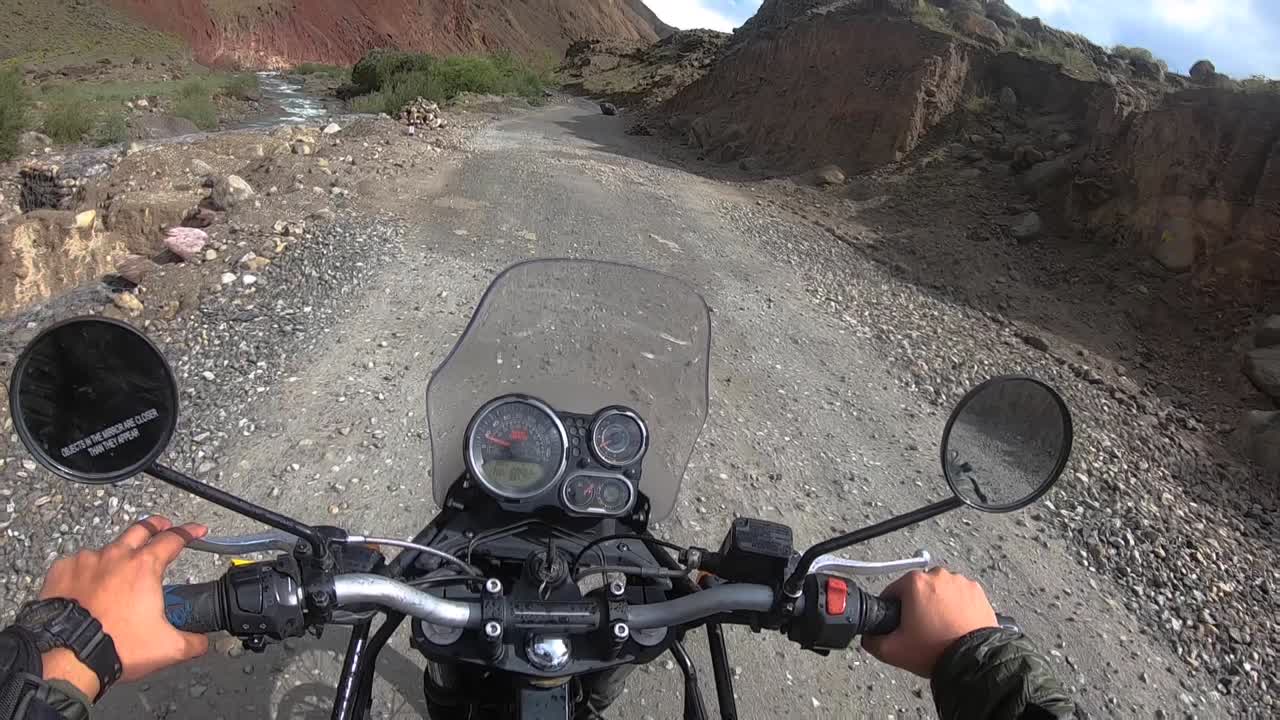 A wide point of view shot of slow riding a bike on a high altitude Himalayan mud road in bright daylight. Bike is driving through colourful scenic, barren mountain ranges of Jammu Kashmir region