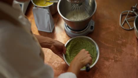 a woman mixes green powder in a bowl while preparing a dessert in the kitchen