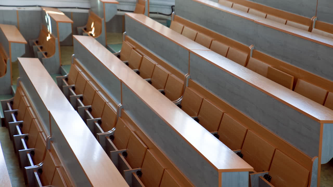 Modern desks in lecture hall. Rows of long wooden tables with vacant seats in the light auditorium at university. Classroom without students.