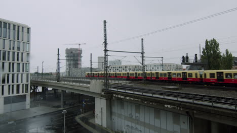 Red-train-is-passing-through-bridge-on-rainy-day-in-Berlin,-Germany