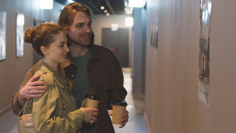 happy couple with a takeaway drink talking together while looking a wall poster at the cinema 2