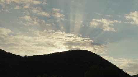 Sonnenstrahlen-Scheinen-über-Einem-Silhouettenhügel-Mit-Goldenem-Licht-Und-Sonnenstrahlen-In-Den-Wolken