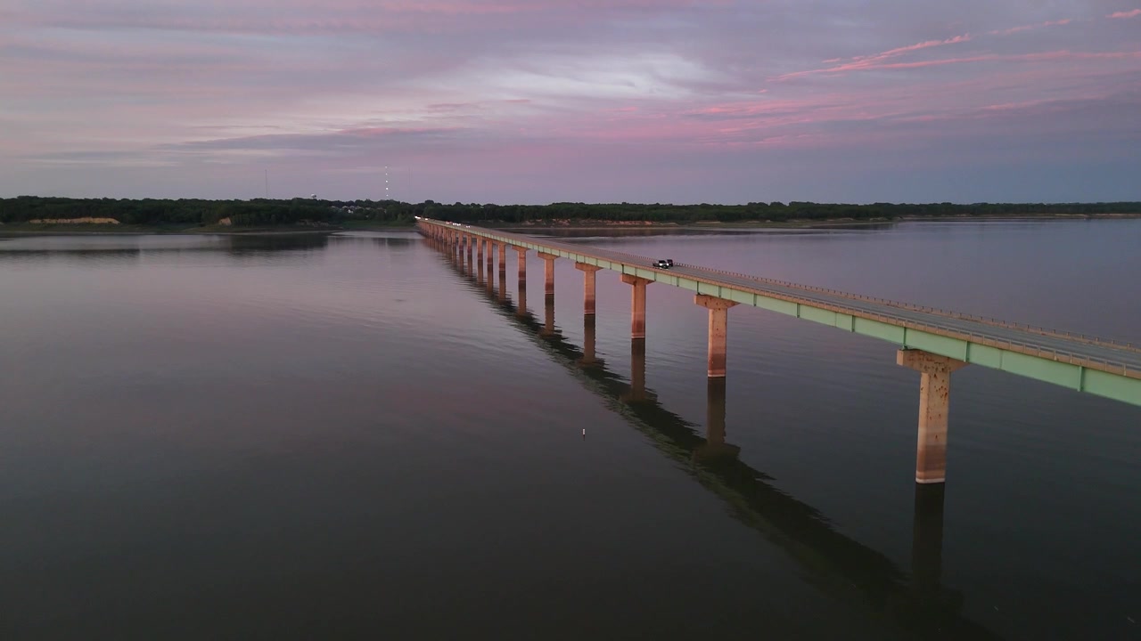 Riprese drone della passerella in legno del Mile Long Bridge che si estende sul tranquillo lago Saylorville in Iowa al tramonto, con pali di legno e un cielo crepuscolare colorato.