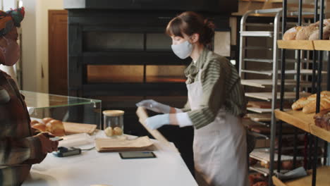 black woman in mask buying bread and paying with phone in bakery