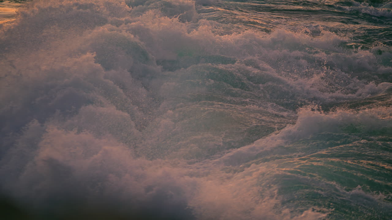 Stříkající vlny pokrývající skálu při západu slunce, detail. Studená mořská voda pěnící večer.