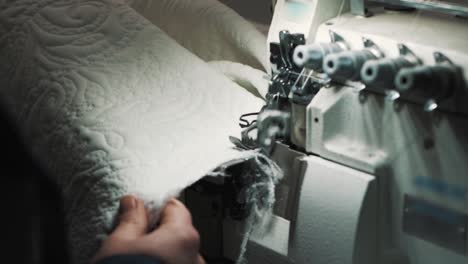 close-up of a sewing machine sewing and simultaneously trimming the edge of white fabric