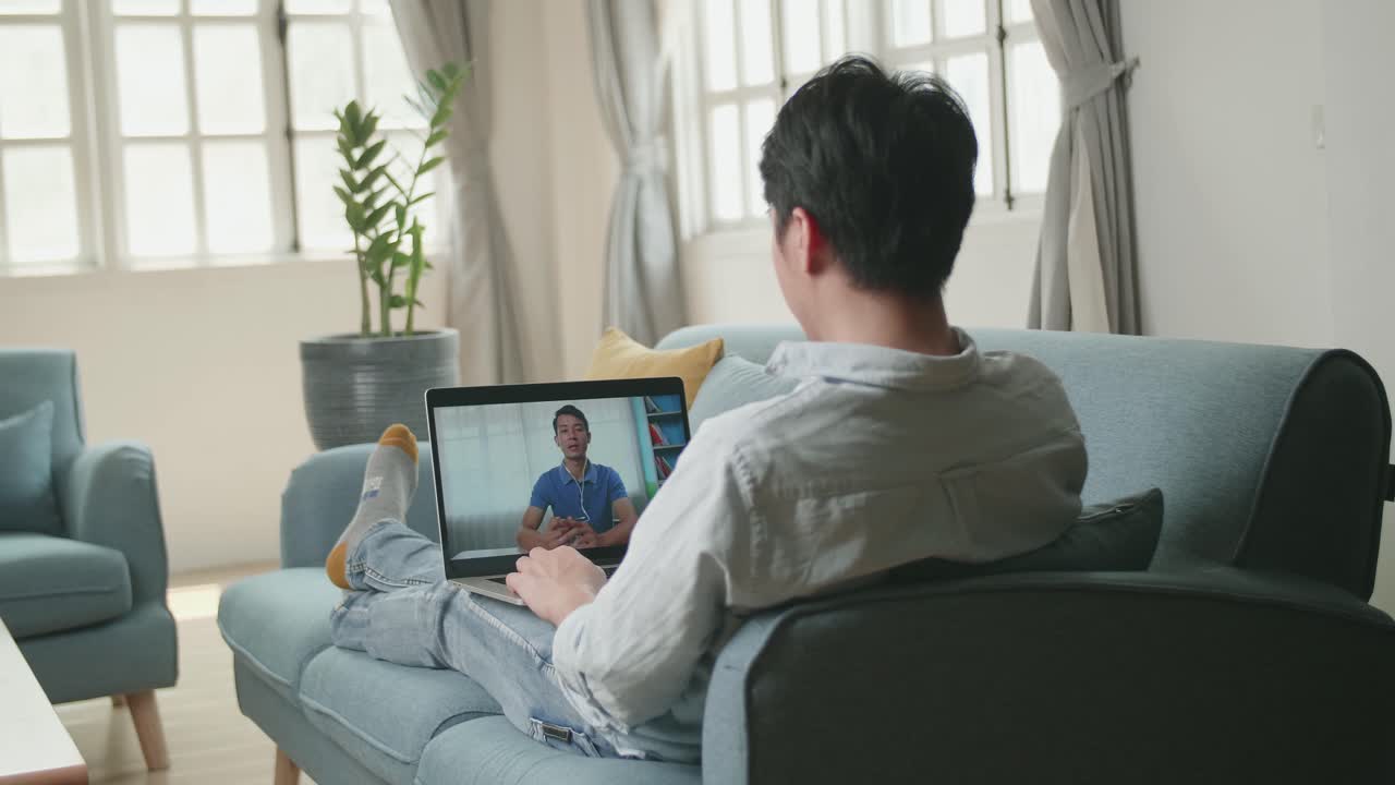 Man Greeting With Colleagues In Video Conference From Laptop At Home Living Room, Video In 4K
