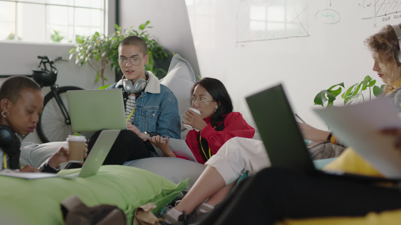 jóvenes estudiantes de negocios estudian compartiendo información haciendo lluvia de ideas para proyectos en grupo usando computadoras portátiles bebiendo café en un lugar de trabajo de oficina relajado y colorido